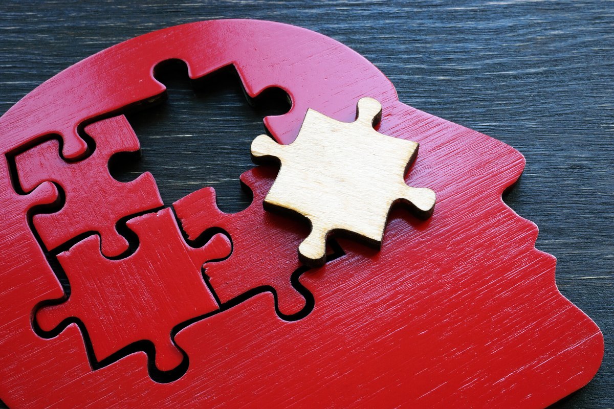 Profilo di testa in legno rosso a forma di puzzle con un tassello chiaro staccato, su tavolo di legno scuro
