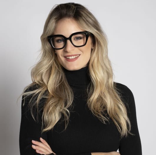 Eleonora Melosi, psicologa, sorridente con occhiali neri, capelli biondi lunghi e dolcevita nero su fondo grigio chiaro